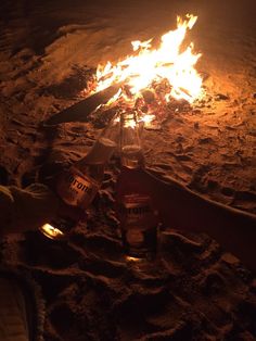 there is a fire pit with beer bottles on the sand and flames in the background