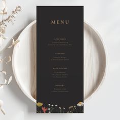 a black and white menu card on a plate with flowers in the middle, next to it is a flower arrangement