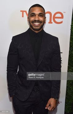 a smiling man in a black suit poses on the red carpet at an evening event