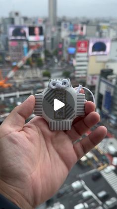 a hand holding a small object in front of a cityscape with lots of buildings