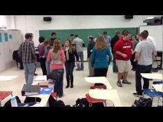 a group of people standing in a room with desks and chairs on the floor