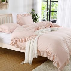 a bed with pink comforters and pillows in a white room next to a window