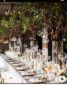 a long table is set up with clear vases and place settings for dinner guests