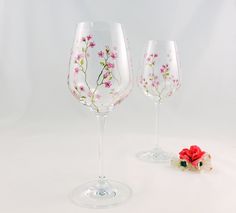 two wine glasses sitting next to each other with flowers painted on the glass and one is empty