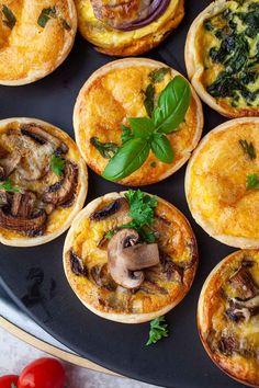 mini quiches with mushrooms, spinach and cheese on a black platter next to tomatoes