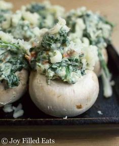 mushrooms covered in spinach and cheese on a black plate