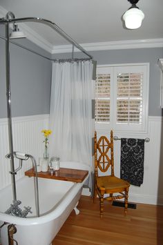 a white bath tub sitting in a bathroom next to a wooden chair and window sill