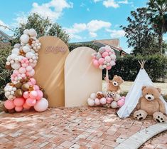 two teddy bears are sitting in front of balloons and a teepee tent on the ground