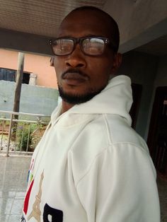 a man wearing glasses standing in front of a building