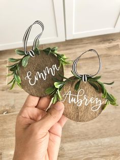 two personalized wooden ornaments with greenery on them, one is hanging from the ceiling