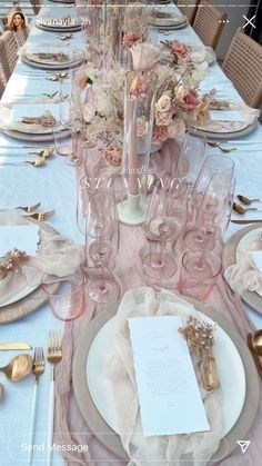 the table is set with white plates and silverware, pink napkins and gold cutlery