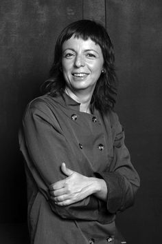 a black and white photo of a woman in a chef's coat with her arms crossed