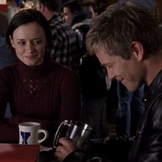 a man sitting next to a woman at a table in front of a coffee cup