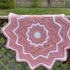 a pink and white crocheted blanket sitting on top of a wooden fence