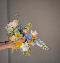 a person holding a bouquet of flowers in their hand with the background gray wall behind them