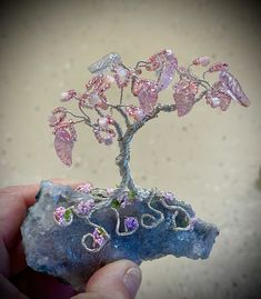 a hand holding a rock with a tree on it and flowers in the rocks next to it