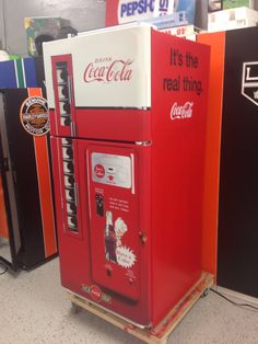 a coca cola machine sitting on top of a wooden pallet next to other vending machines