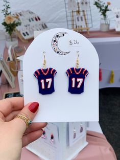 a pair of earrings featuring a football jersey and the number 17 on it in front of a tent