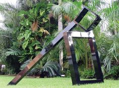 a metal sculpture sitting in the middle of a lush green field next to palm trees