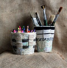 two cups with pens and pencils are sitting on a couch next to each other