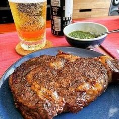 a steak on a blue plate next to a glass of beer and some condiments