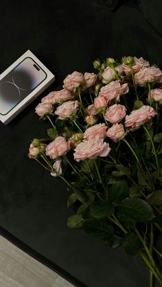 a bunch of pink roses sitting on top of a table next to a cell phone