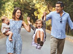 a man and woman walking down the street with two small children in their arms while holding hands