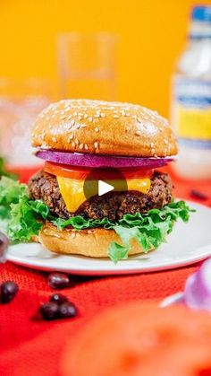 a hamburger sitting on top of a white plate next to a bottle of water and an orange table cloth