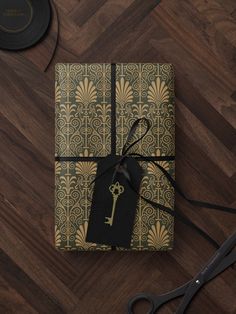 a gift wrapped in gold and black paper with a key on it next to a pair of scissors