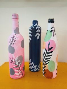 three painted bottles sitting on top of a yellow table