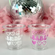 two shot glasses with the words bride and babe painted on them next to pink feathers