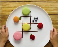 a white plate topped with desserts on top of a wooden table next to two hands