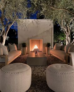 an outdoor fireplace with wicker furniture and potted trees in the background at night