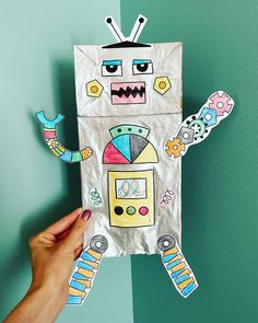 a person holding up a paper cut out of a robot with various stickers on it