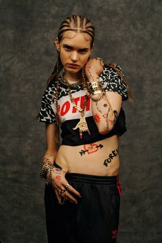 a young woman with tattoos on her body and hands around her neck, standing in front of a dark background