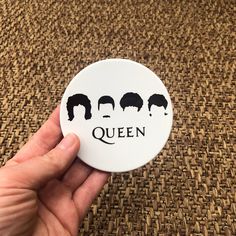 a hand holding a button with the words queen and four men's heads on it