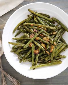 a white bowl filled with cooked green beans and topped with toasted almonds on a wooden table