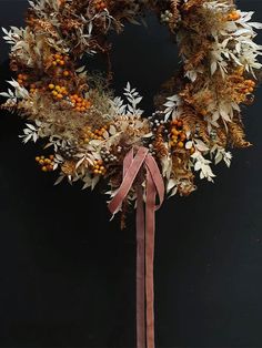 a wreath with oranges and berries hanging on a black wall next to a pink ribbon