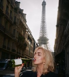 a woman drinking from a bottle in front of the eiffel tower, paris