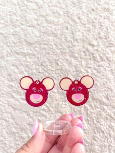 a pair of red earrings with pink mouse ears on them, hanging from clear acrylic earwires