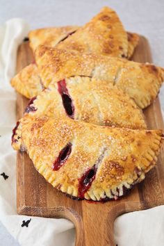 three pastries sitting on top of a wooden cutting board next to a white cloth