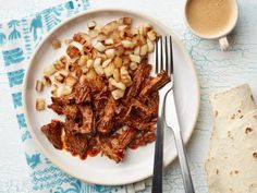 a white plate topped with meat and potatoes next to a cup of coffee