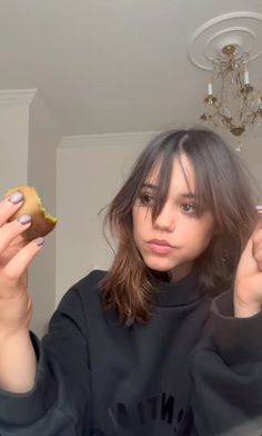 a woman holding a donut in her right hand and looking at the camera with both hands