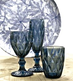 three blue glass goblets sitting on a table next to a plate with flowers