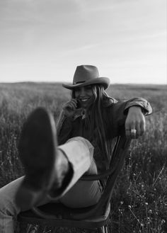 a woman sitting in a chair talking on a cell phone while wearing a cowboy hat