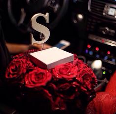 a red rose covered cake with the letter s on it's stand in a car