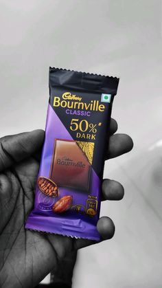 a hand holding a bar of chocolate with nuts in it and the wrapper is dark