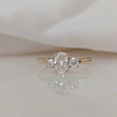 a three stone diamond ring sitting on top of a white cloth