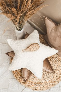 a white star shaped pillow sitting on top of a bed next to a vase filled with dry grass