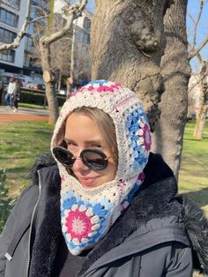 a woman wearing sunglasses and a crocheted hat standing in front of a tree